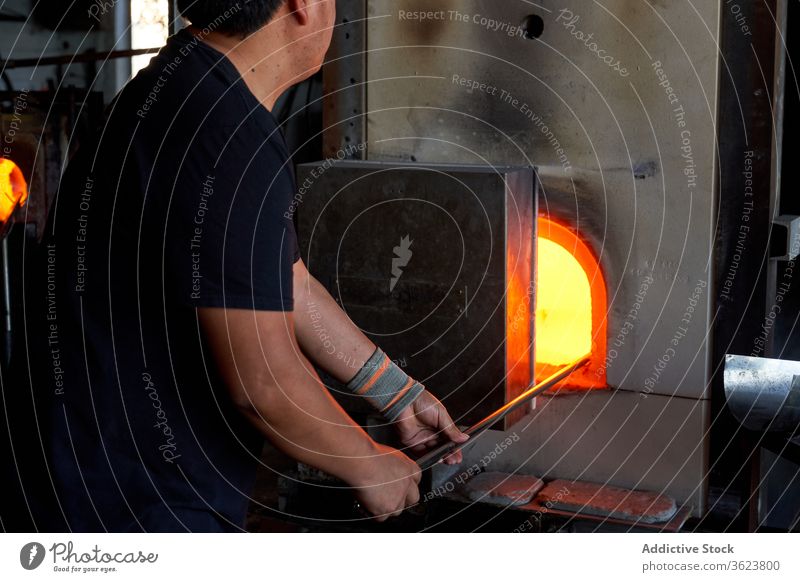Glass blower melting glass in furnace man blowpipe workshop hot craft equipment craftsman skill industry production manufacture small business flame