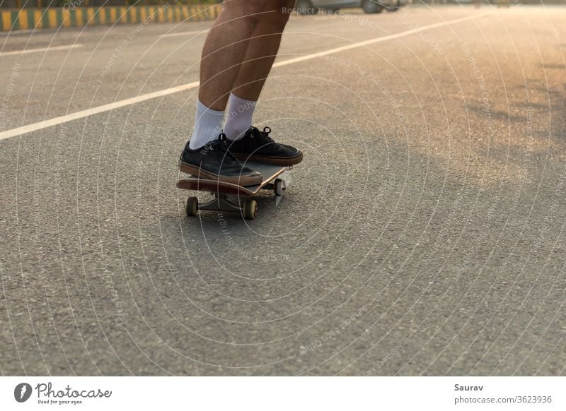 Close-up Shot of a Young Teenager's feet wearing Ripped Black Sneakers on his Skateboard cruising on an Empty Street while the White Line on the Road compliments his White Socks and also acts as a Leading Line in the Direction he is Moving.