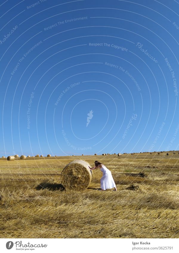 Woman Pushing Hay Bale Hay bale Bale of straw rolling Clear sky Meadow Field Harvest Grain Straw white dress Summer Agriculture