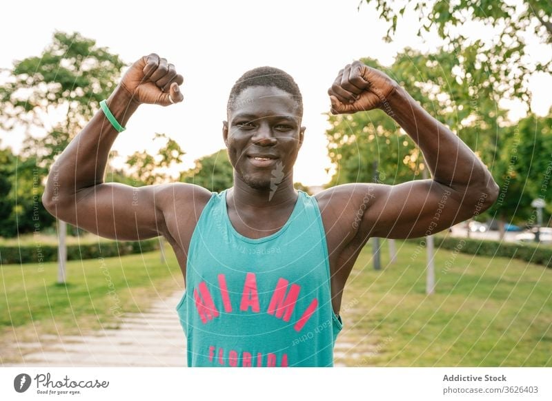 Athletic black man exercising at the park african cheerful muscular fitness smiling strong flexing body muscle biceps happy arms athlete strength lifestyle