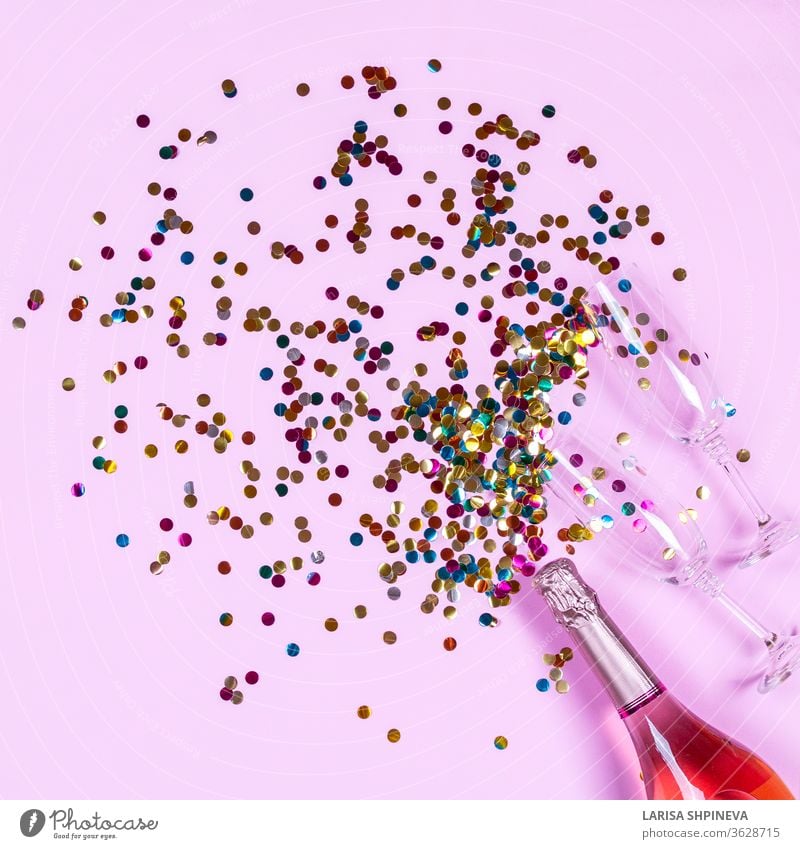 A bottle of champagne, glasses and splashing golden confetti on a pink background. Romantic party creative trendy composition. top view, lay-up, copy room Party
