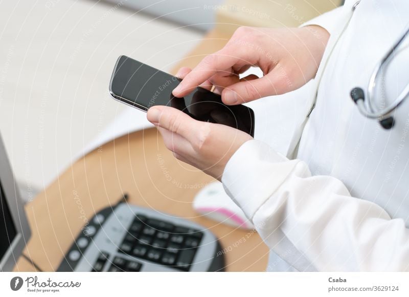 A female doctor texting on smartphone woman cellphone using typing message hand holding touching mobile closeup medical office nurse healthcare hospital