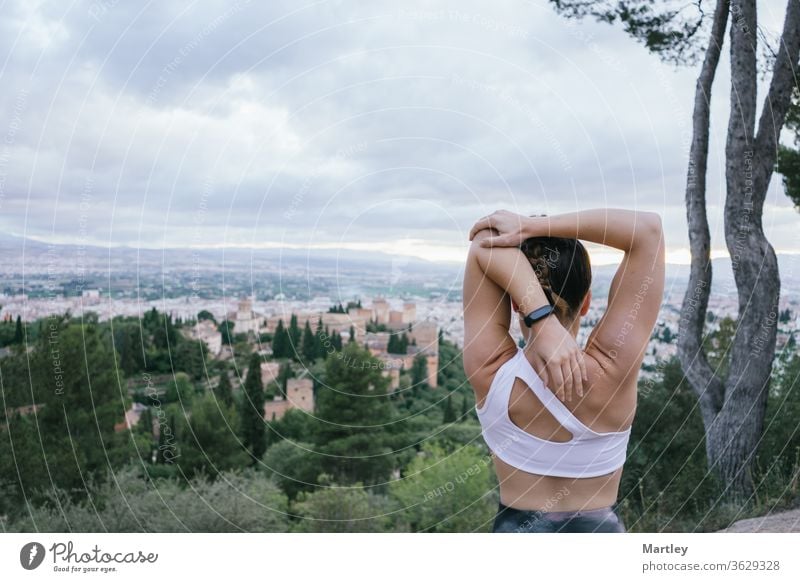 Fit woman on vacation doing stretching exercises over the city in the summer afternoon in front of the Alhambra. fitness lifestyle alhambra sunset spain