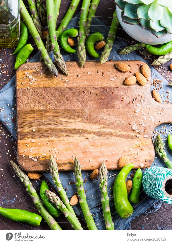 Wooden chopping board with asparagus, nuts frame wooden food salt seeds dark brown textured backdrop napkin healthy plant based cooking concept background pink