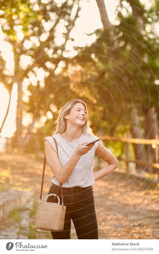 Happy woman with smartphone standing in park cheerful using happy enjoy browsing young female trendy lifestyle gadget device rest chill positive social media