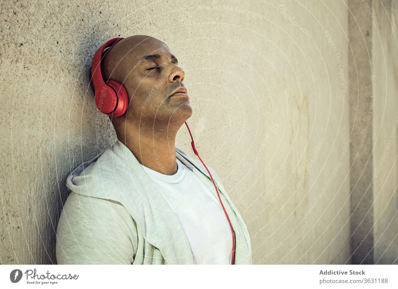 Relaxed man listening to music in headphones enjoy peaceful relax harmony song city male ethnic sound chill device lean stone wall street carefree entertain