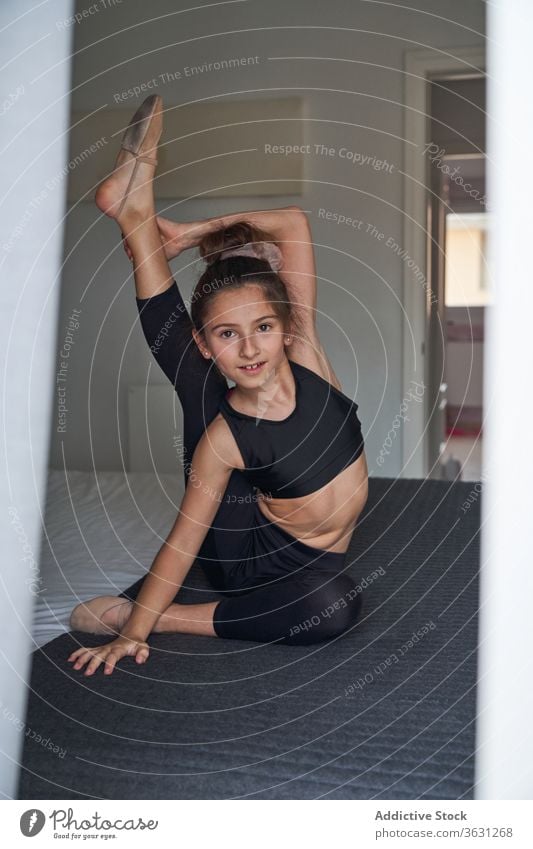Flexible acrobatic girl sitting on bed flexible gymnastic leg behind neck home energy teen healthy activity calm body stretch slim practice bedroom laugh