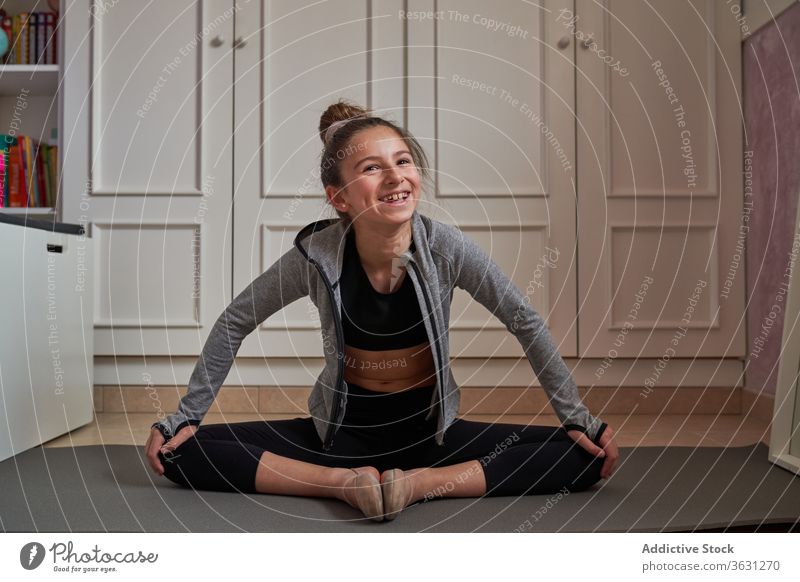 Cheerful girl sitting in lotus pose while stretching gymnastic laugh mat home child artist happy contemporary posture training choreography apartment flexible