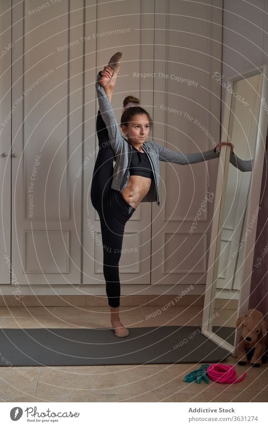 Acrobatic girl doing splits standing in front of mirror gymnastic stretch flexible home leg raised slim balance dancer reflection mat child artist contemporary
