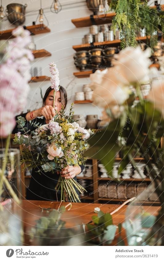Florist with bouquet of flowers working in shop floristry woman arrange create concentrated bloom blossom cheerful compose designer decorative female creative
