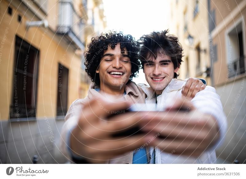 Cheerful gay couple taking selfie on smartphone homosexual hug together street lgbt mobile phone using multiracial diverse ethnic relationship cellphone photo