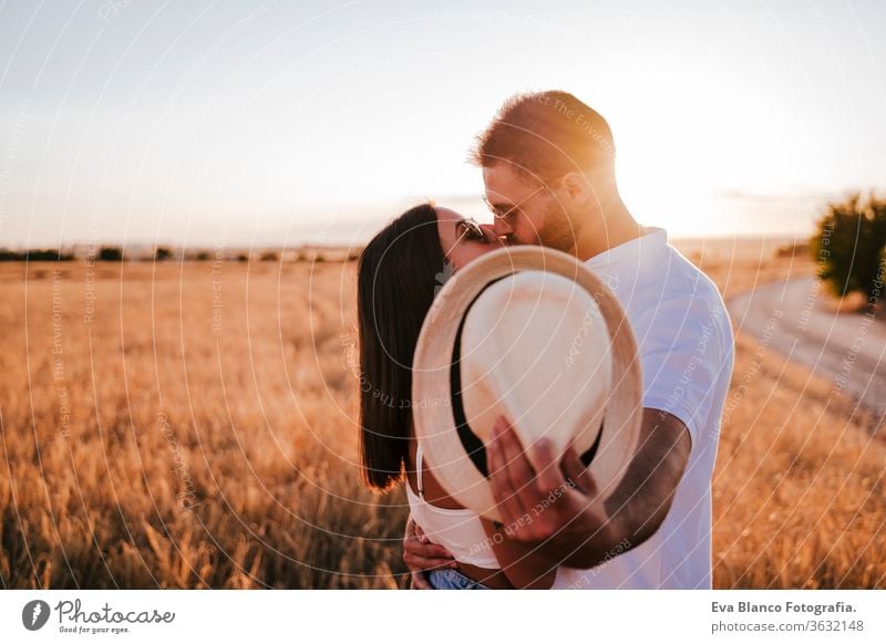 young couple kissing and hiding with a hat in a yellow field at sunset. Love and Summer time cover hide love man woman together togetherness daytime lifestyle