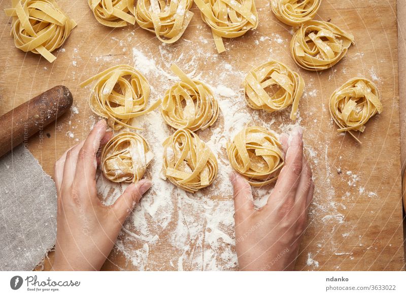 raw fettuccine pasta and two female hands are cooking pasta preparation preparing rolled round spaghetti table traditional uncooked vegetarian wheat white woman