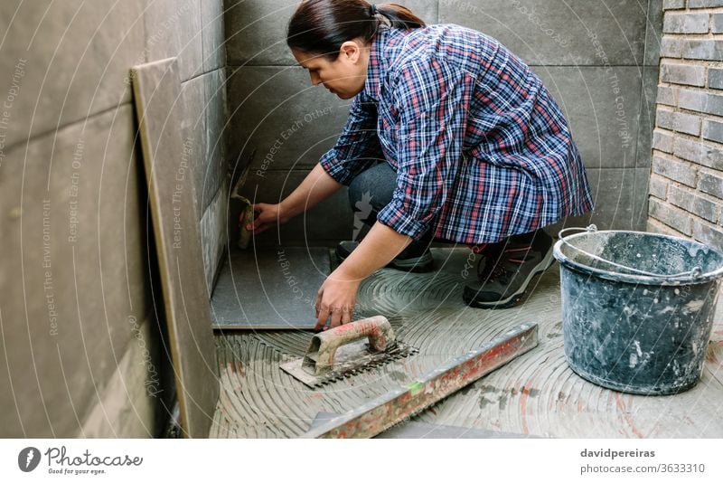 Female manual worker laying a new tile floor mason woman reform light knocks spatula tap glazed terrace female handyman placing diy workman concrete tiling