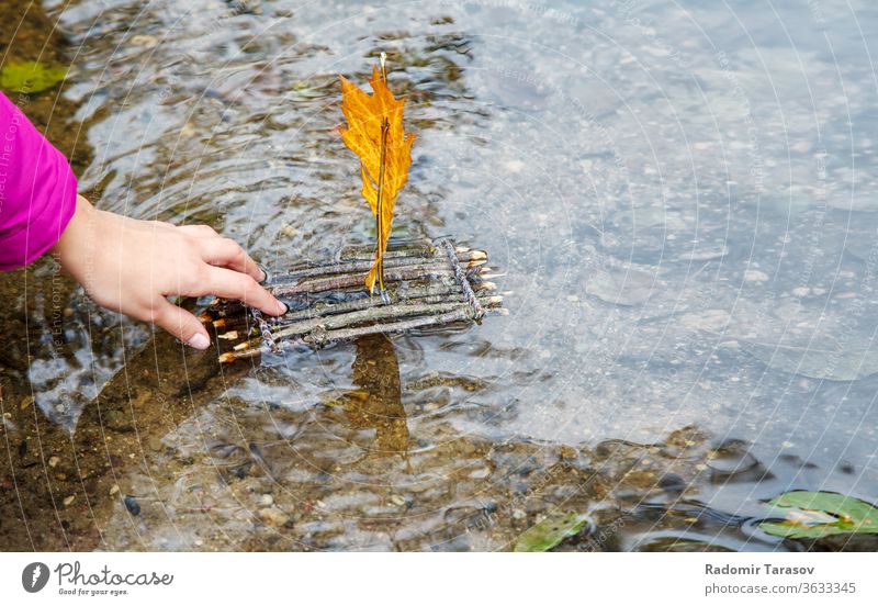 teen girl puting wooden handmade small toy raft in the creek on late autumn day. hand closeup sail water simple nature object background river landscape concept