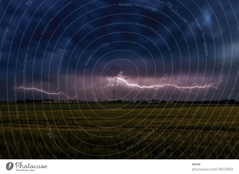 Thunderstorm atmosphere with lightning over wheat fields with cloudy sky and view of Inningen near Augsburg View copy space dark gigantic gloomy landscape