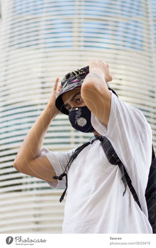 A Young Man outdoors in a protective face mask to prevent Corona virus infection adjusting his floral printed bucket cap and wearing a bag pack during Global pandemic.
