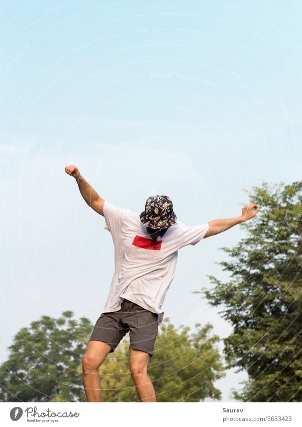 A Young Adult wearing a protective mask to avoid Coronavirus infection while doing an Ollie stunt on his Skateboard outdoors ion an empty road. summer