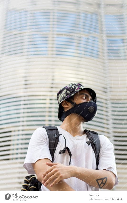 A Young Man outdoors in a protective face mask to prevent Corona virus infection wearing a floral printed bucket cap and a bag pack during Global pandemic.