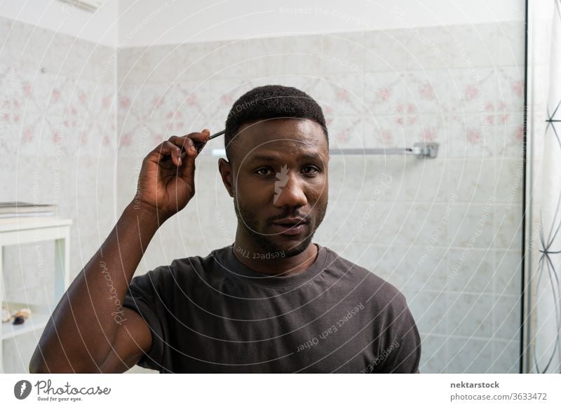 Young Black Man Combing Hair Looking at Camera combing hair face hairstyle man 1 person African ethnicity lifestyle 20-30 years old handsome domestic life