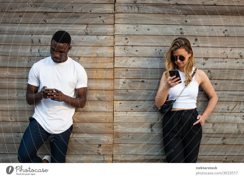 Young Man and Woman with Cool Attitudes Using Phones Outside woman smartphone lifestyle wall 2 people male female young man young woman handsome attractive