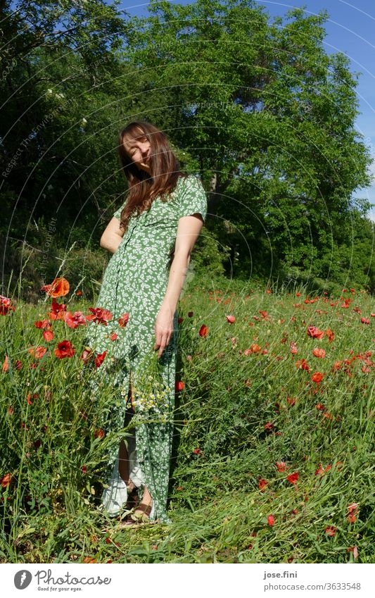 Woman stands in a long summer dress in a poppy field with a bouquet of flowers in her hand and smiles mischievously. Summer dress Dress romantic Calm Dream