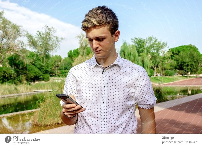 Young blond male using a cell phone outdoors 1 mobile young person teenage smartphone guy man people street fashion city lifestyle modern standing technology