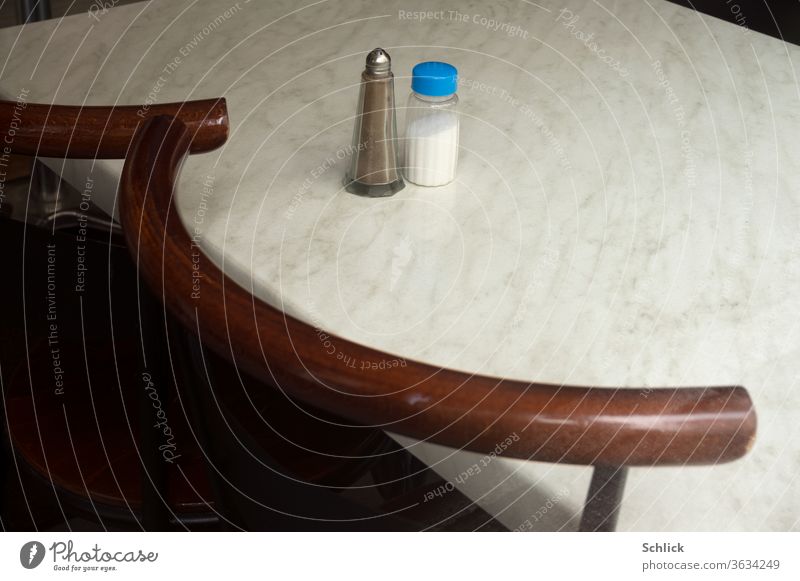 Salt and pepper stand alone on a white marble table two chairs are pushed to the table Pepper Salt caster Pepper caster Marble White marble slab Table Lonely