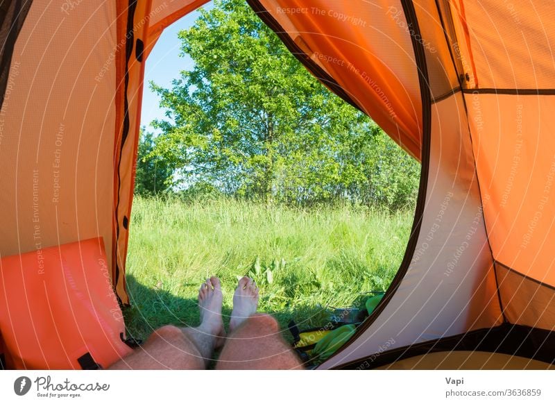 Man resting inside orange tent camp vacation camping legs nature view grass foot people recreation forest tree landscape adventure tourism summer travel hiking