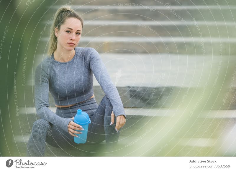 Contemplative sportswoman resting on stairs with bottle after workout athlete break water think contemplative healthy solitude fit peaceful sportswear wellbeing
