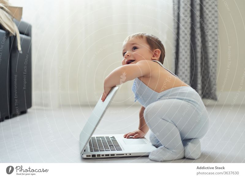 Cheerful baby playing with laptop at home happy using toddler gadget modern childhood lifestyle little alone kid cheerful device netbook cute innocent excited
