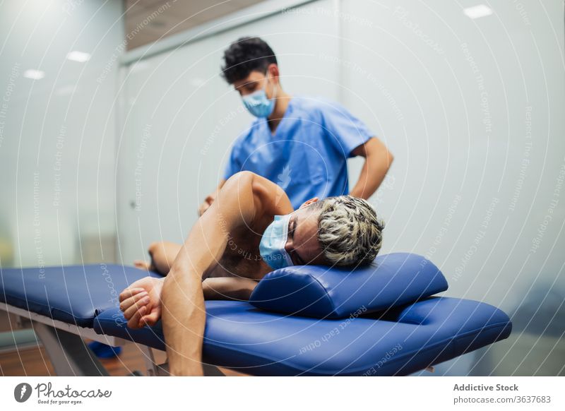 Orthopedist with mask examining the back of sportsman with mask during medical checkup orthopedist patient recovery examine stretching professional osteopathy