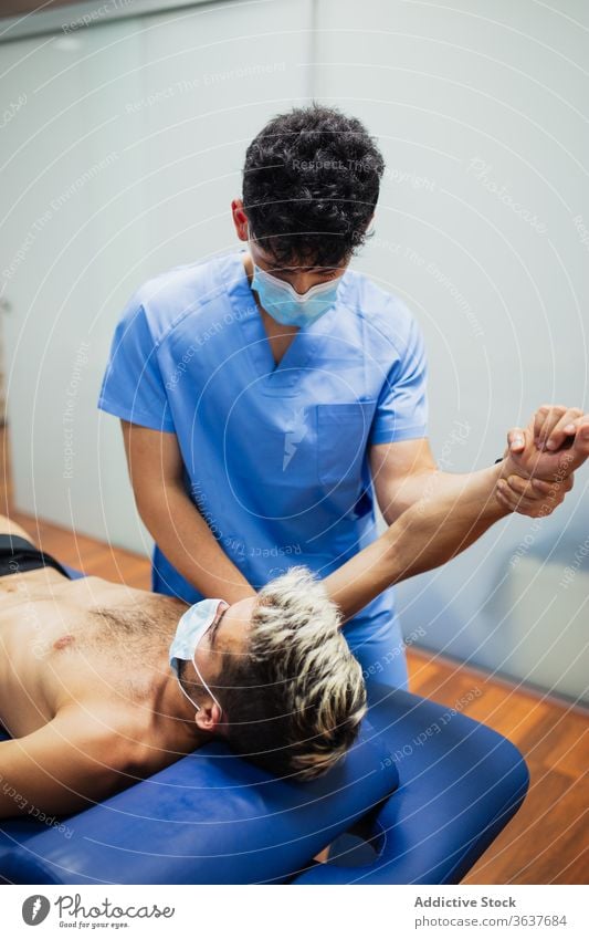 Orthopedist with mask stretching arm of sportsman with mask during medical checkup orthopedist patient recovery examine professional osteopathy aid health care