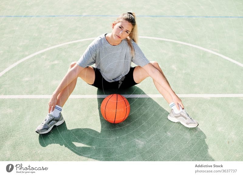 Female basketball player sitting on sports ground woman exercise warm up training prepare court female workout activity game lifestyle wellbeing young power