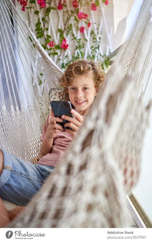 Boy taking selfie on smartphone sitting in hammock boy weekend childhood toothy smile comfort rest using gadget device cellphone harmony idyllic content happy