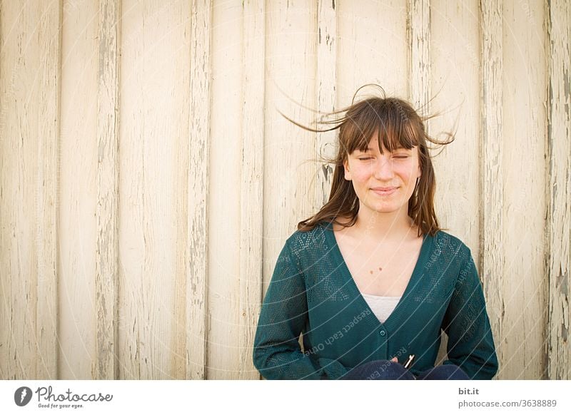 Teenagers stand with closed eyes in front of a bright wooden wall and enjoy the wind in their hair. Youth (Young adults) teenager Meditation Mediterranean girl