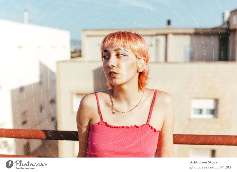 Woman standing on a rooftop looking away woman millennial rainbow expressive pink hair different female summer railing city lean freedom urban unemotional style