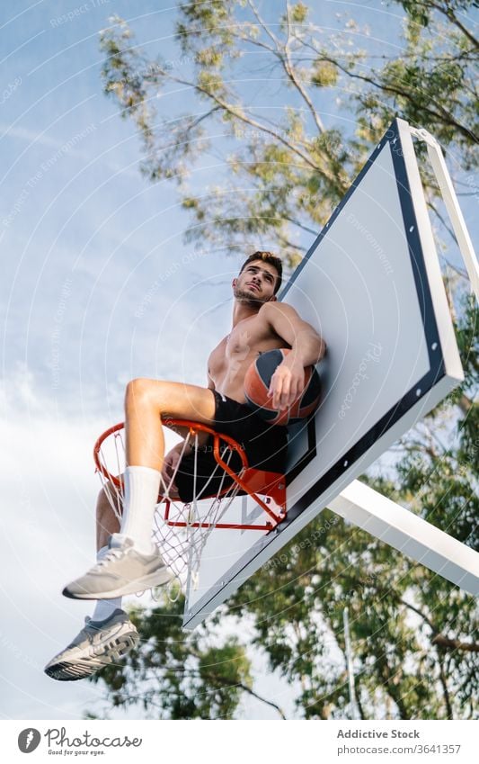 Basketball player sitting on hoop on playground basketball man sportsman training game healthy male handsome professional activity exercise sportswear athlete