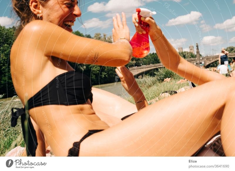 Two young women taking a bath, having fun and splashing themselves with water from a spray bottle bathe Summer Spray bottle cooling Water girl sunbathe Bikini