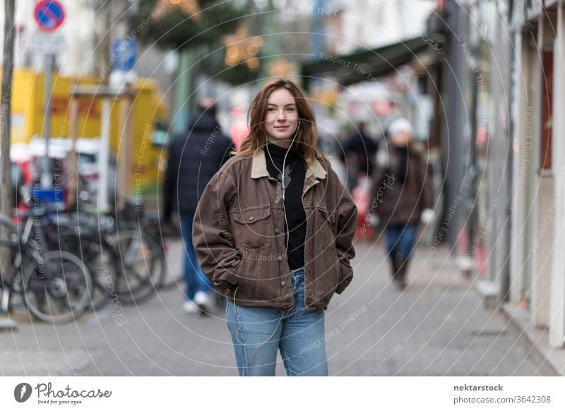 Young Woman in Jeans and Jacket Listening to Earphones on Sidewalk caucasian ethnicity woman female earphones audio music listening sidewalk street