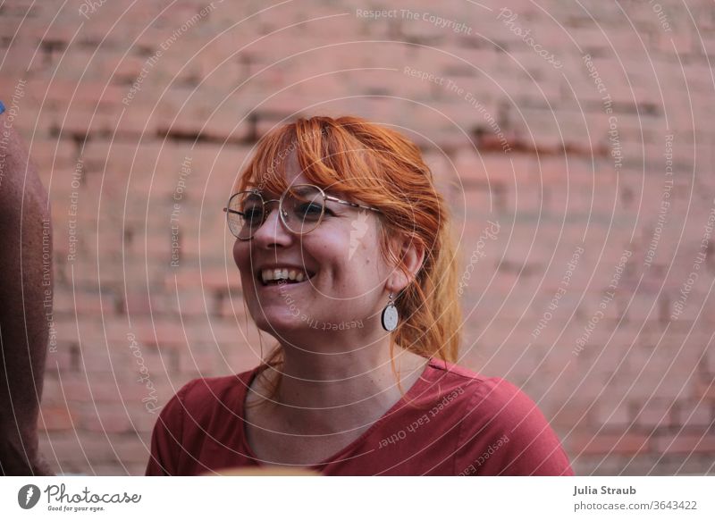 Laughing woman with rust red hair and stylish glasses sits in front of a brick wall Woman Laughter radiation Copper Copper colours Eyeglasses