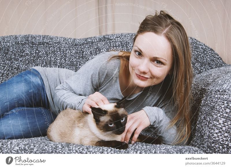 happy young woman relaxing on sofa with cat pet girl affection couch stroke stroking cuddle cuddling petting female adult blonde casual jeans denim smile