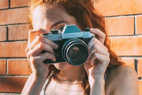 young woman holds an analog camera and looks through the viewfinder antiquated antique antiquity classic classical click close up electronic equipment film
