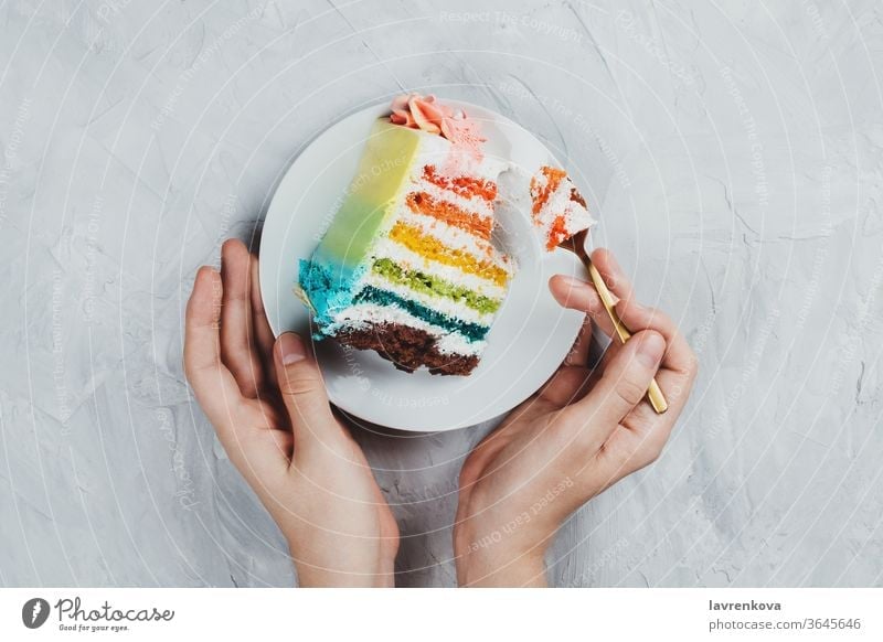 Flat lay of rainbow vegan cake piece in woman's hands on grey background diet gift pink snack tasty happy girl pastry birthday view top spoon flatlay flat lay