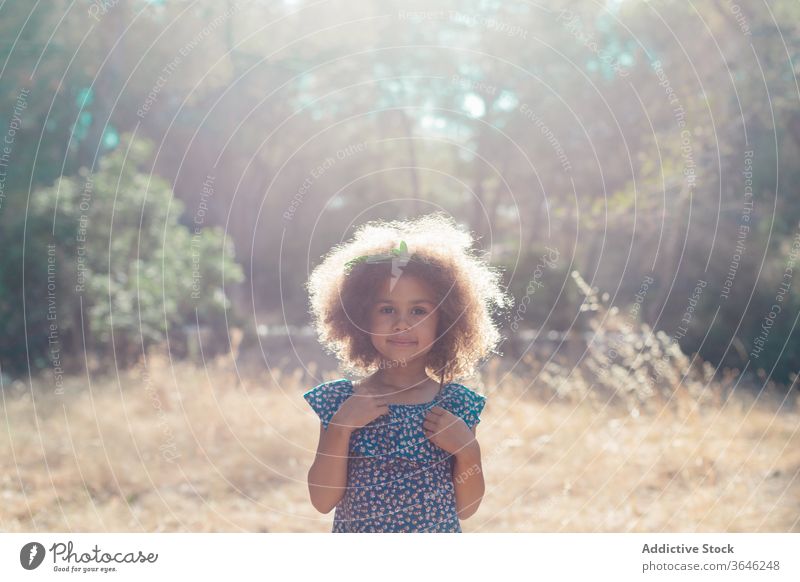 Serious little mulatto girl on blurred nature background black child serious portrait calm adorable summer style outfit unemotional curly hair cute sunlight