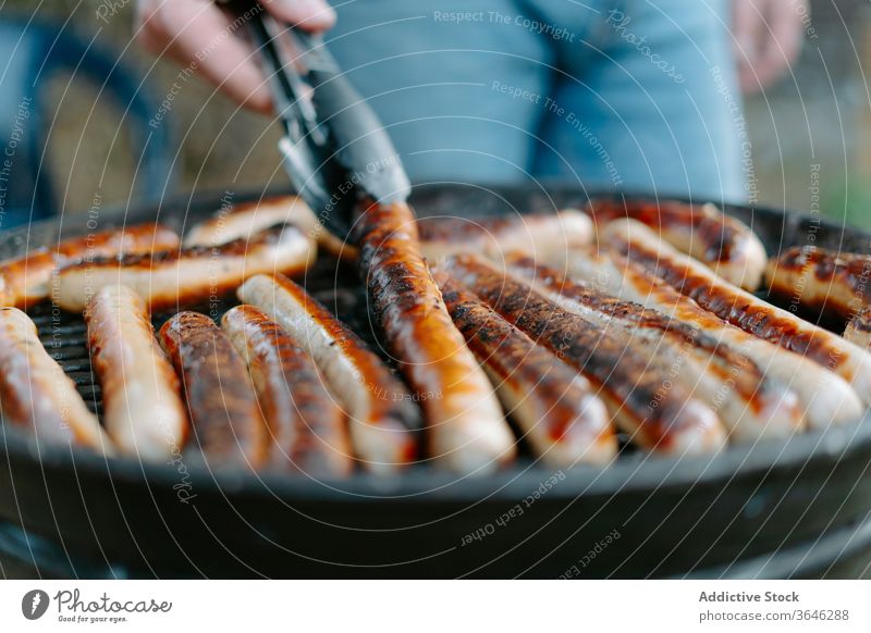 Crop person grilling sausages on barbecue pan delicious backyard tasty cook tong dinner summer roast bbq yummy cuisine meat hot fresh lunch prepare dish nature
