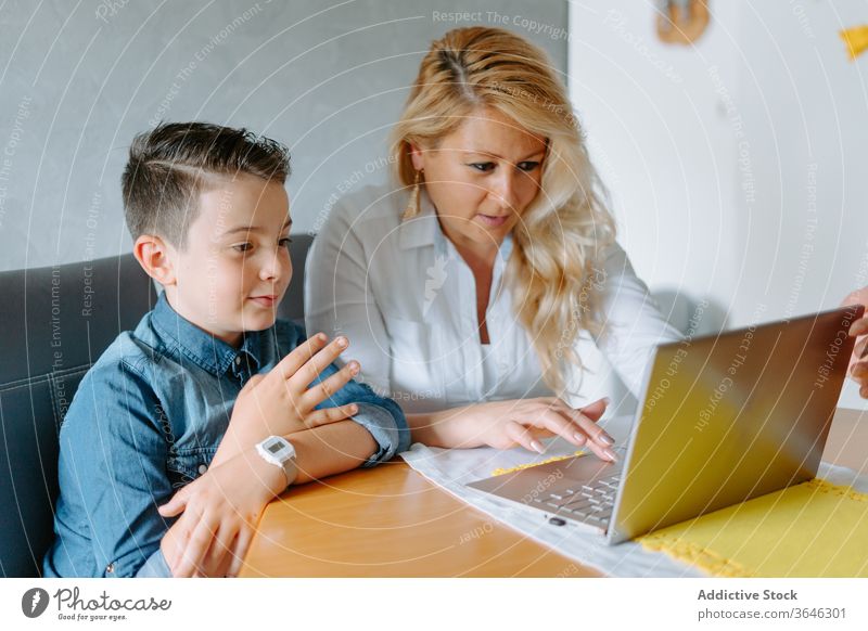 Positive mother with son using laptop modern home schooling content browsing living room parent tutor study teacher lesson table netbook cozy at home together