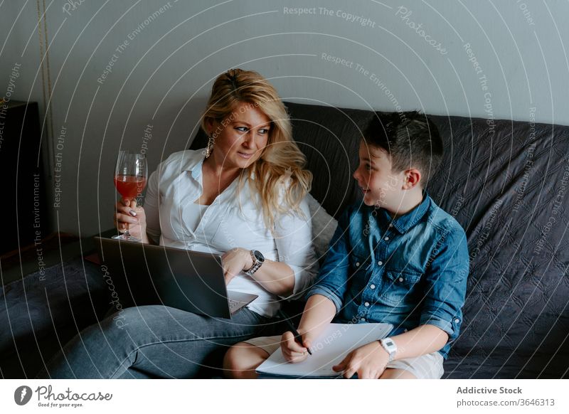 Positive mother and son resting on sofa with laptop using modern content happy smile glass cheerful study sheet cocktail relax paper browsing parent netbook