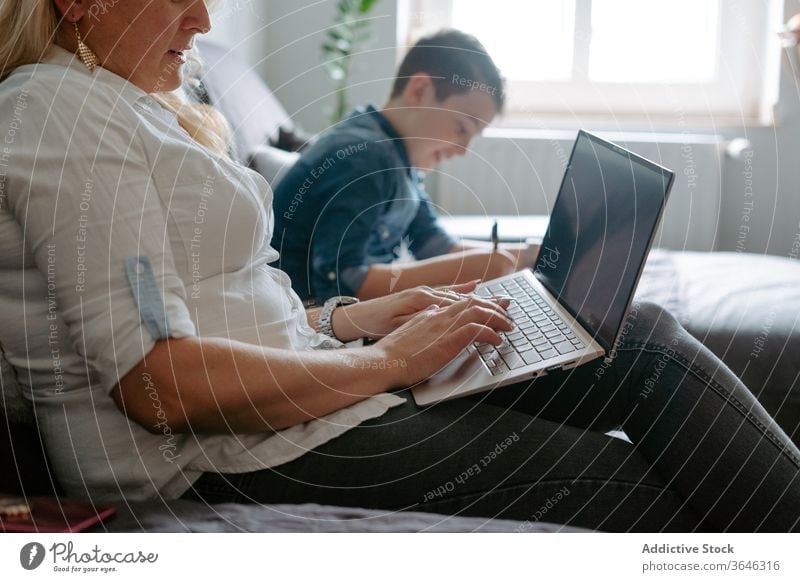 Positive mother and son resting on sofa with laptop using modern content happy smile glass cheerful study sheet relax paper browsing parent netbook cozy at home