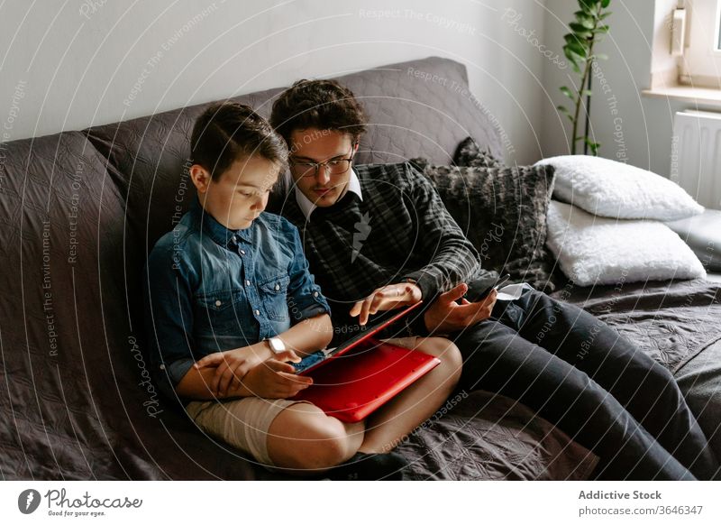 Schoolboy with brother browsing tablet on comfy sofa siblings using gadget contemporary relax rest chat legs crossed surfing connection cozy together point
